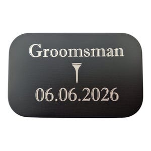 May include: A black rectangular plaque with rounded corners. The word "Groomsman" is at the top, with a golf tee symbol below it. The date "06.06.2026" is at the bottom in a white, elegant font.