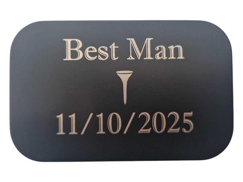May include: A black rectangular plaque with rounded corners, featuring the words "Best Man" above a golf tee symbol and the date "11/10/2025" in a light beige color. The text is centered on the plaque.