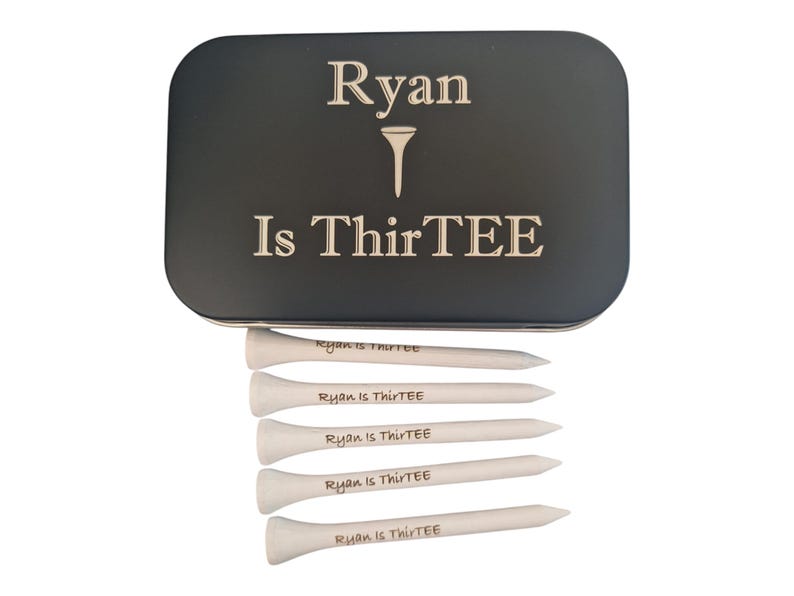 Op de afbeelding: Een zwarte metalen golf tee box met de tekst "Ryan Is ThirTEE" in het wit. Daaronder zes witte golf tees, elk met "Ryan is ThirTEE" erop gedrukt. Een cadeau set voor een golfer.