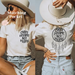 May include: Two white t-shirts with the text "Chase Dreams Not People" on the front and back. The back design features a dreamcatcher with feathers. The model is wearing denim shorts and a white cowboy hat.