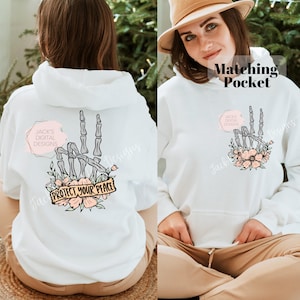 May include: White hoodie featuring a skeleton hand making the peace sign with flowers and a banner that reads "Protect Your Peace".