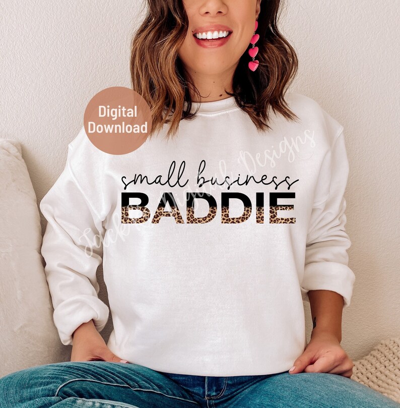K&ouml;nnte beinhalten: Wei&szlig;er Pullover mit dem Text "small business BADDIE" in schwarzer Schrift. Das Wort "BADDIE" ist in einem Leopardenmuster gedruckt.