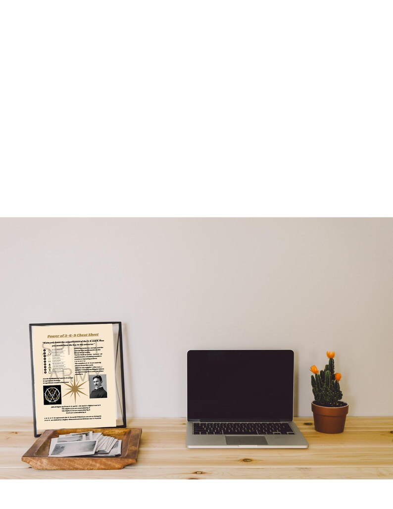 May include: A framed print titled Power of 3-6-9 Cheat Sheet featuring text, a star graphic, and a portrait of Nikola Tesla, displayed next to a silver laptop and a small green cactus in a brown pot on a light wood surface.