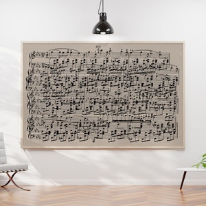 May include: A black and white sheet music print in a light brown frame hangs on a white wall. A white chair with a tufted back sits in front of the print. A small white table with a potted plant sits on the right side of the image.
