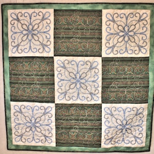 May include: A quilt with a green background and nine white squares. Each square has a blue and black embroidered design of a stylized flower.