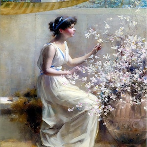 May include: A woman in a white dress with a blue sash sits in a room with a window and a large pot of white flowers. The flowers are in bloom and the woman is reaching out to touch them.