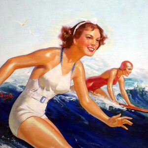 Op de afbeelding: Twee vrouwen in vintage badkleding rijden op surfplanken op golven. De vrouw op de voorgrond draagt een witte badpak met een blauwe riem en een wit hoofdband. De vrouw op de achtergrond draagt een rode badpak en een rode badmuts. De zee is blauw en de lucht is lichtblauw.