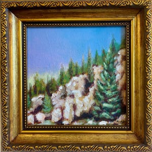 May include: An oil painting depicting a mountain landscape with green trees and rocky cliffs under a blue sky. The artwork is presented in a gold, ornate frame, enhancing the natural scene with a touch of elegance.