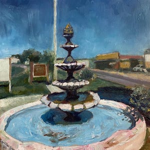 May include: A black cast iron fountain with a blue water basin and a pink rim. The fountain has four tiers and a pineapple-shaped finial. The fountain is in front of a flagpole with an American flag.