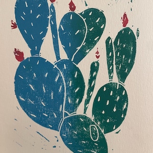 Könnte beinhalten: Ein Linolschnitt eines Feigenkaktus. Der Kaktus ist in Türkis- und Grüntönen dargestellt, mit kleinen roten Blüten. Der Druck hat ein strukturiertes, handgemachtes Aussehen, mit weißen Details und einem weißen Hintergrund.