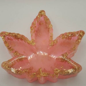 May include: A pink leaf-shaped dish with gold flecks throughout. The dish is made of resin and has a glossy finish.