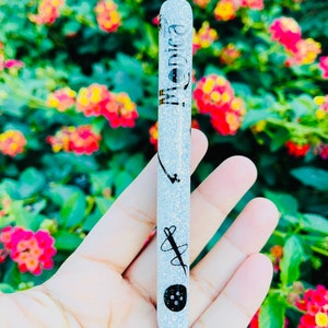 K&ouml;nnte beinhalten: Ein silberner Glitzer-Stift mit schwarzer Tinte und einer schwarzen Kappe. Der Stift hat ein schwarzes Design aus Nadel und Faden mit einem Knopf auf dem Schaft. Der Stift tr&auml;gt die Aufschrift "Monica" auf dem Schaft.