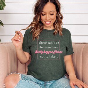 Pode incluir: Uma camiseta verde escura com o texto "These can't be the same men Dolly begged Jolene not to take..." em branco. O texto "Dolly begged Jolene" est&aacute; em rosa.