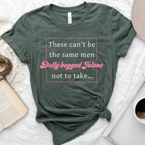 Pode incluir: Uma camiseta verde com o texto "These can't be the same men Dolly begged Jolene not to take..." impresso em branco. O texto "Dolly begged Jolene" est&aacute; em rosa e estilizado.