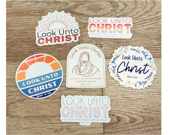 May include: Five colorful stickers with the text "Look Unto Christ" and a scripture reference. The stickers feature different designs, including a sunrise, a floral wreath, and a simple line drawing of Jesus.