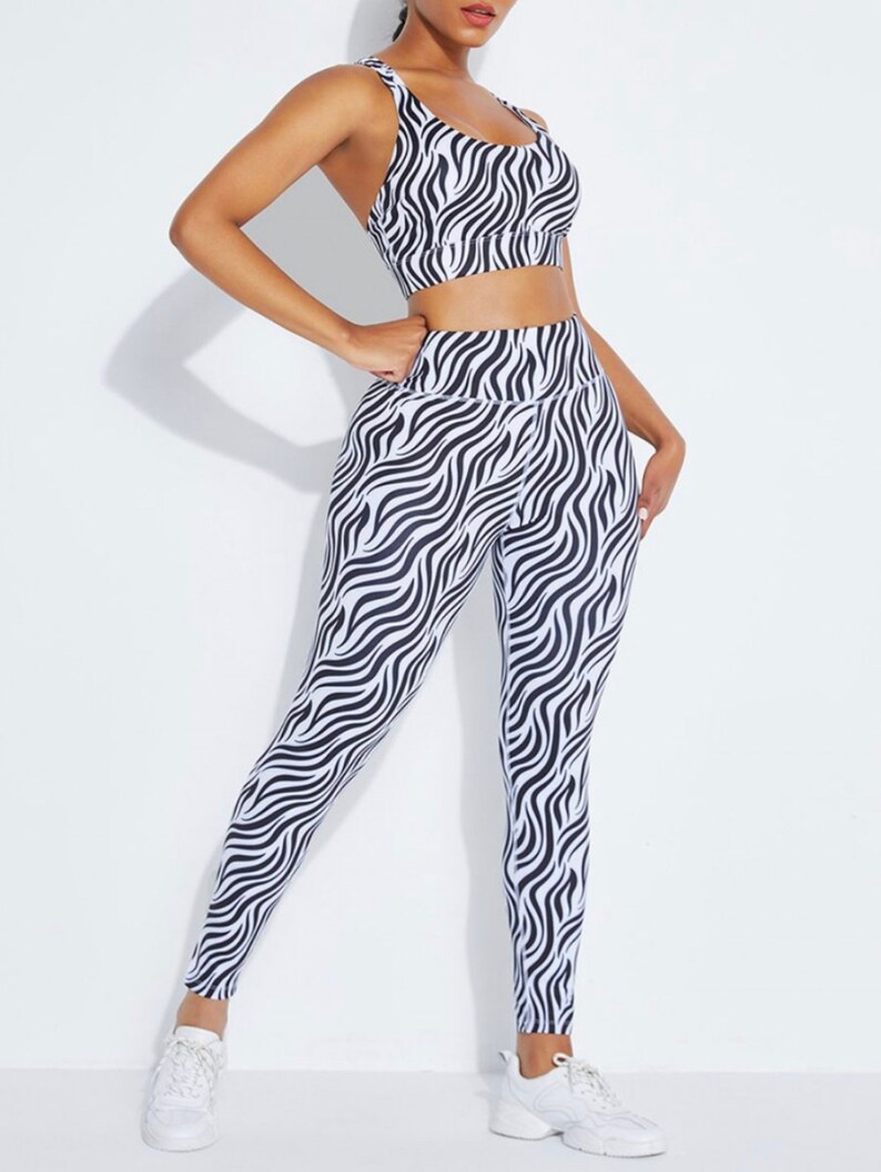 K&ouml;nnte beinhalten: Ein zweiteiliges Sport-Set mit einem schwarz-wei&szlig;en Zebramuster. Das Set besteht aus einem Sport-BH mit d&uuml;nnen Tr&auml;gern und einer hoch taillierten Leggings. Das Outfit ist f&uuml;r Fitnessaktivit&auml;ten konzipiert und besteht aus einem dehnbaren Material.