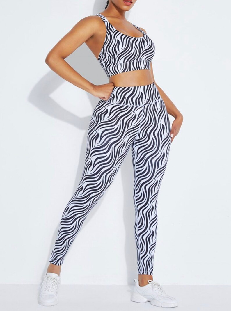K&ouml;nnte beinhalten: Ein zweiteiliges Sport-Set, bestehend aus einem Sport-BH und Leggings. Das Set ist mit einem schwarz-wei&szlig;en Zebra-Streifenmuster versehen. Der Sport-BH hat einen Rundhalsausschnitt und d&uuml;nne Tr&auml;ger. Die Leggings sind hoch tailliert.