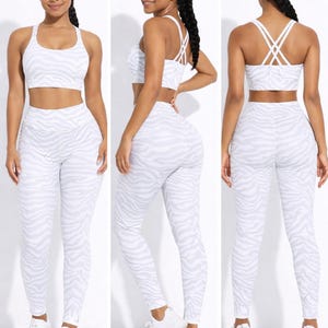 K&ouml;nnte beinhalten: Ein wei&szlig;-graues Sport-BH- und Leggings-Set mit Zebrastreifen. Der BH hat einen Rundhalsausschnitt und die Leggings sind hoch tailliert. Das Set wird mit wei&szlig;en Turnschuhen kombiniert. Das Model tr&auml;gt das Set in drei verschiedenen Posen.