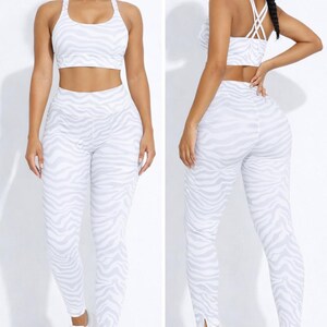 K&ouml;nnte beinhalten: Zweiteiliges Sport-Set mit wei&szlig;-grauem Zebra-Print. Das Set besteht aus einem Sport-BH und einer hoch taillierten Leggings. Das Model tr&auml;gt wei&szlig;e Turnschuhe.