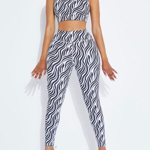 K&ouml;nnte beinhalten: Ein passendes Sport-Set mit Zebra-Print-Design. Das Set beinhaltet einen Sport-BH mit gekreuztem R&uuml;cken und eine hoch taillierte Leggings. Das schwarz-wei&szlig;e Muster erzeugt einen auff&auml;lligen Look. Das Model tr&auml;gt wei&szlig;e Turnschuhe.