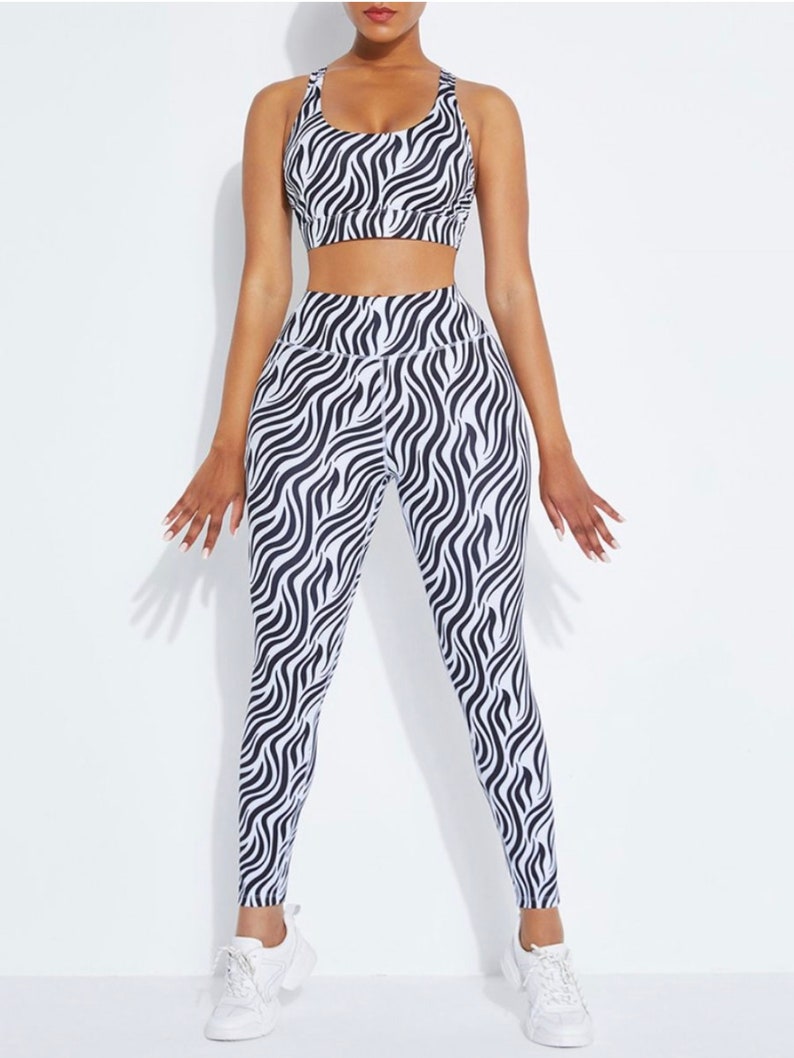 K&ouml;nnte beinhalten: Ein passendes Sport-Set mit Zebra-Print-Design. Das Set beinhaltet einen Sport-BH mit gekreuztem R&uuml;cken und eine hoch taillierte Leggings. Das schwarz-wei&szlig;e Muster erzeugt einen auff&auml;lligen Look. Das Model tr&auml;gt wei&szlig;e Turnschuhe.