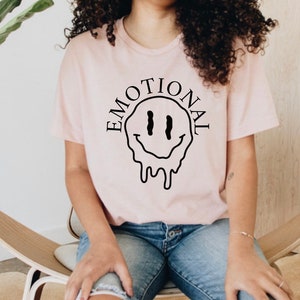 May include: A pink t-shirt with a black dripping smiley face and the word "EMOTIONAL" written around it.