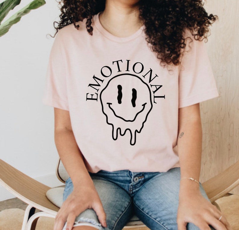 May include: A pink t-shirt with a black dripping smiley face and the word "EMOTIONAL" written around it.