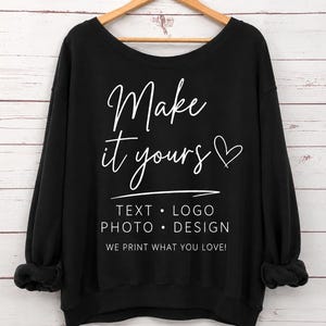 May include: A black long-sleeve sweatshirt featuring white text that reads Make it yours with a heart icon, followed by the words TEXT • LOGO, PHOTO • DESIGN, and the phrase WE PRINT WHAT YOU LOVE! in a clean, sans-serif font style.