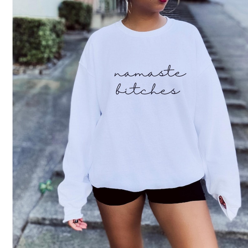 May include: White sweatshirt with the text "namaste bitches" printed in black.