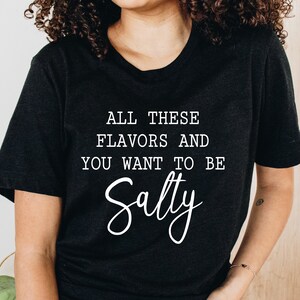 May include: A black t-shirt with white text that reads "All these flavors and you want to be Salty".