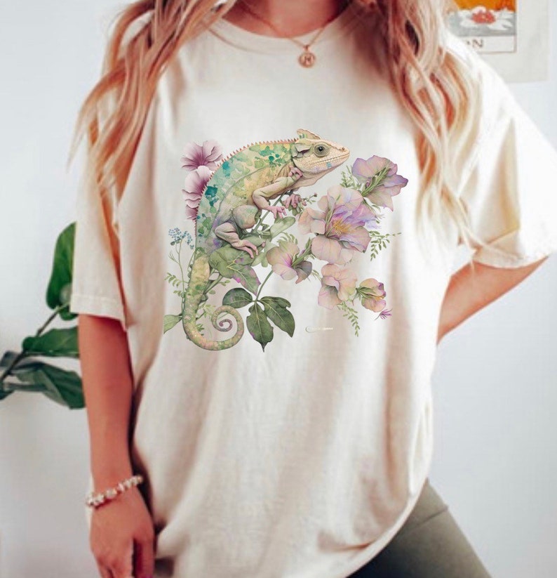 May include: A white t-shirt featuring a green chameleon and pink flowers printed on the front.