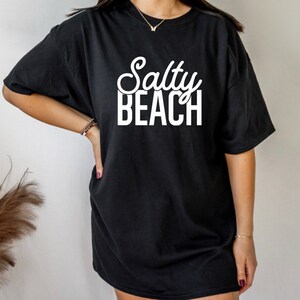 May include: Black oversized t-shirt with white text that reads "Salty Beach".