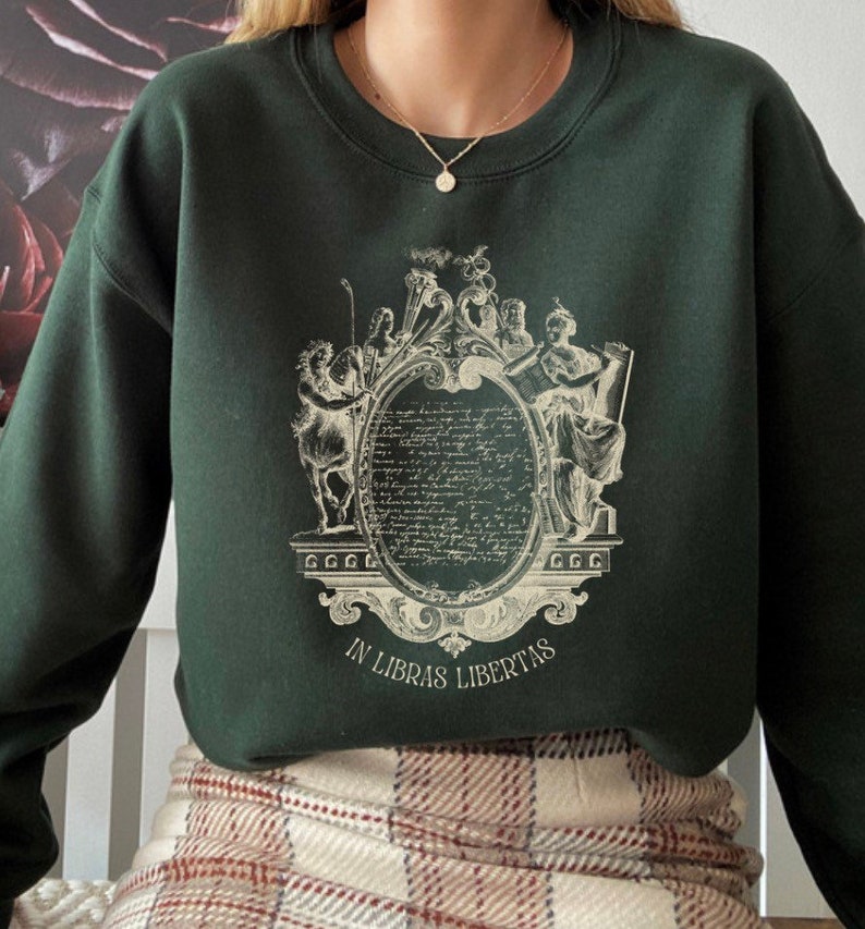 May include: A dark green sweatshirt with a vintage-style graphic print of a crest featuring figures and the text "In Libras Libertas".