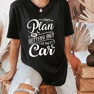 Może przedstawiać: Czarny T-shirt z białym napisem "Nie planowałem wysiadać z samochodu".