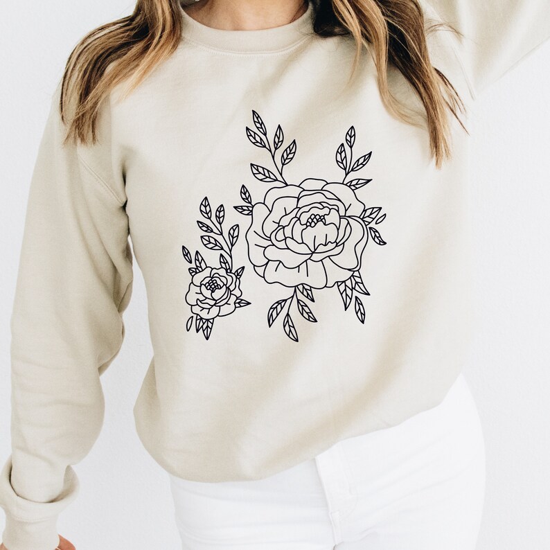 K&ouml;nnte beinhalten: Ein beiger Pullover mit einer schwarzen Umrandung eines Blumendesigns mit zwei Pfingstrosen und Bl&auml;ttern.