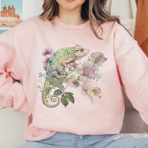 May include: A pink sweatshirt featuring a green chameleon and watercolour flowers printed on the front.