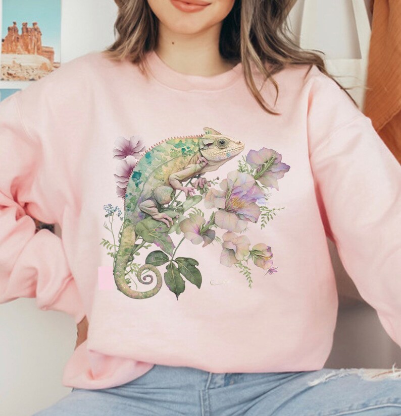 May include: A pink sweatshirt featuring a green chameleon and watercolour flowers printed on the front.