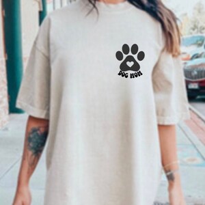 May include: A white t-shirt with a black paw print and a heart inside the print. The text "Dog Mom" is below the paw print.