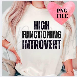 Könnte beinhalten: Cremefarbenes T-Shirt mit dem Text "HIGH FUNCTIONING INTROVERT" in fetter, verwaschener schwarzer Schrift. Ein rosa Herz mit "PNG FILE" befindet sich in der oberen rechten Ecke. Das Shirt ist ein lässiger Stil.