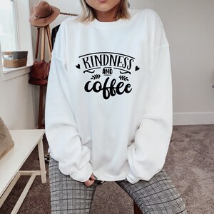 May include: White sweatshirt with black text that reads "Kindness and coffee" with two small hearts and a leaf design.