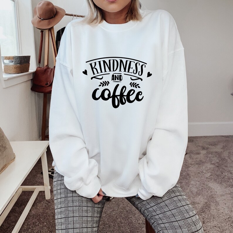 May include: White sweatshirt with black text that reads "Kindness and coffee" with two small hearts and a leaf design.