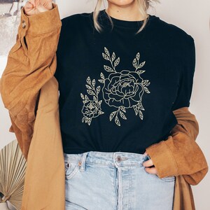 K&ouml;nnte beinhalten: Ein schwarzes T-Shirt mit einer wei&szlig;en Umrandung von zwei Blumen und Bl&auml;ttern.