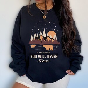 May include: Black sweatshirt with a graphic of a forest scene with two bears, a sunset, and stars. The text on the sweatshirt reads "If you never go you will never -know-"