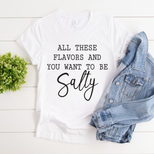 May include: White t-shirt with the text "All these flavors and you want to be Salty" in black lettering.