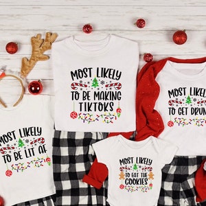 May include: Four white t-shirts with Christmas lights and text that reads "Most Likely To Be Making TikToks", "Most Likely To Be Lit AF", "Most Likely To Eat The Cookies", and "Most Likely To Get Drunk".