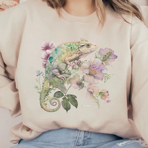 May include: A beige sweatshirt featuring a watercolour illustration of a green chameleon perched on pink flowers.
