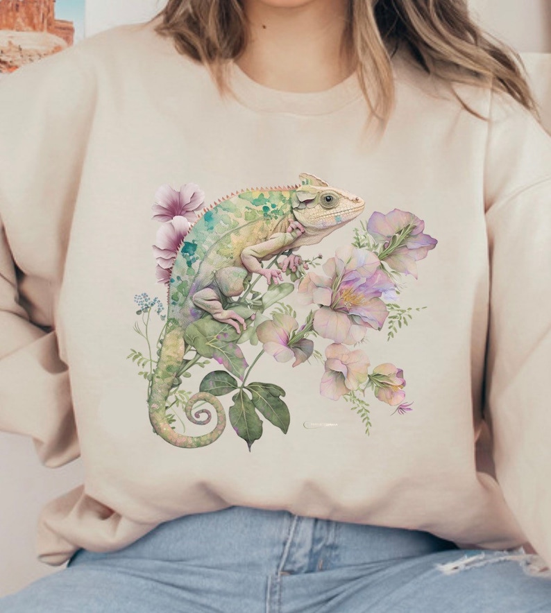 May include: A beige sweatshirt featuring a watercolour illustration of a green chameleon perched on pink flowers.