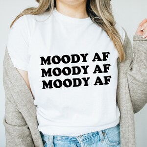 May include: White t-shirt with the text "MOODY AF" repeated three times in black.
