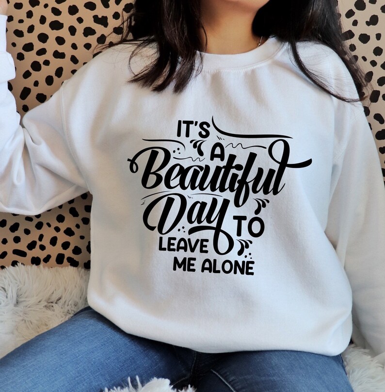 May include: White sweatshirt with the phrase "It's a Beautiful Day to Leave Me Alone" in black script. The sweatshirt is a crew neck style and is made of a soft material. The text is centered on the front of the sweatshirt.