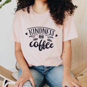 May include: A pink t-shirt with the text "Kindness and coffee" in black lettering. The text is in a stylized font with hearts and floral accents.